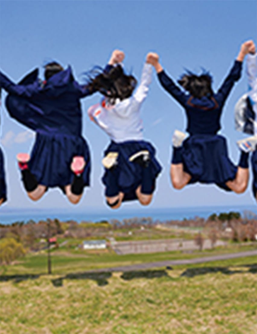 広い青空の下で手をつないでジャンプする制服姿の学生たち