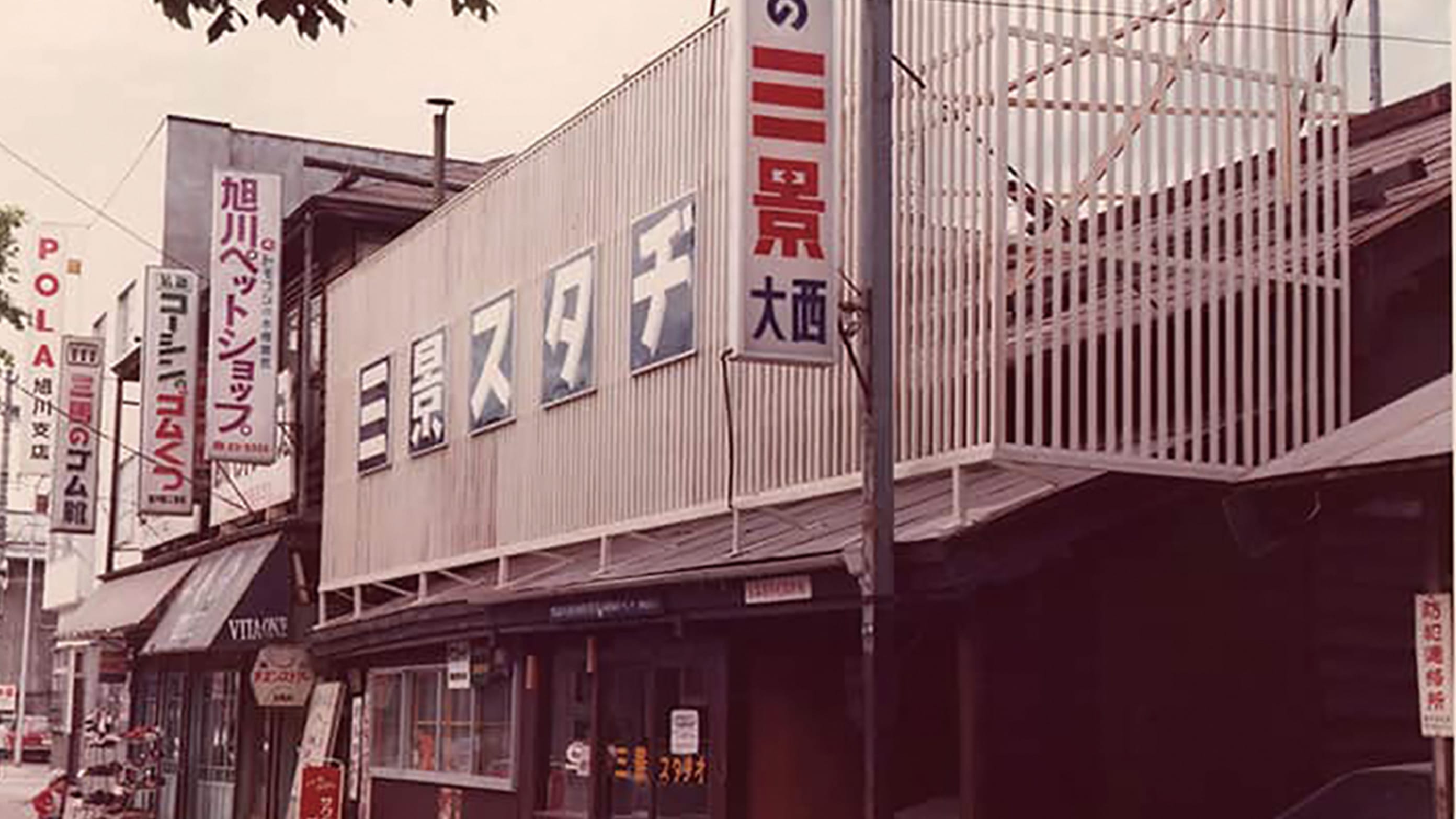 昭和時代の商店街、手前に三景スタジオの大きな看板があり、周囲には旭川ペットショップやポーラ旭川支店などの看板が並んでいる街並み