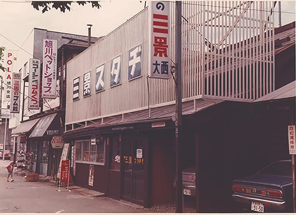 昭和時代の商店街、手前に三景スタジオの大きな看板があり、周囲には旭川ペットショップやポーラ旭川支店などの看板が並んでいる街並み